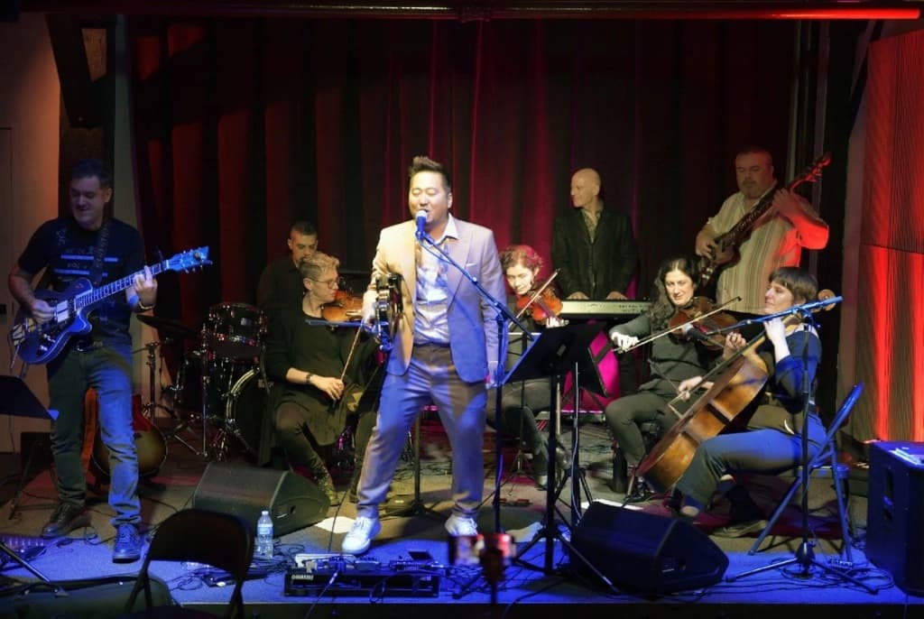 Live performance with band and string section under dramatic stage lighting